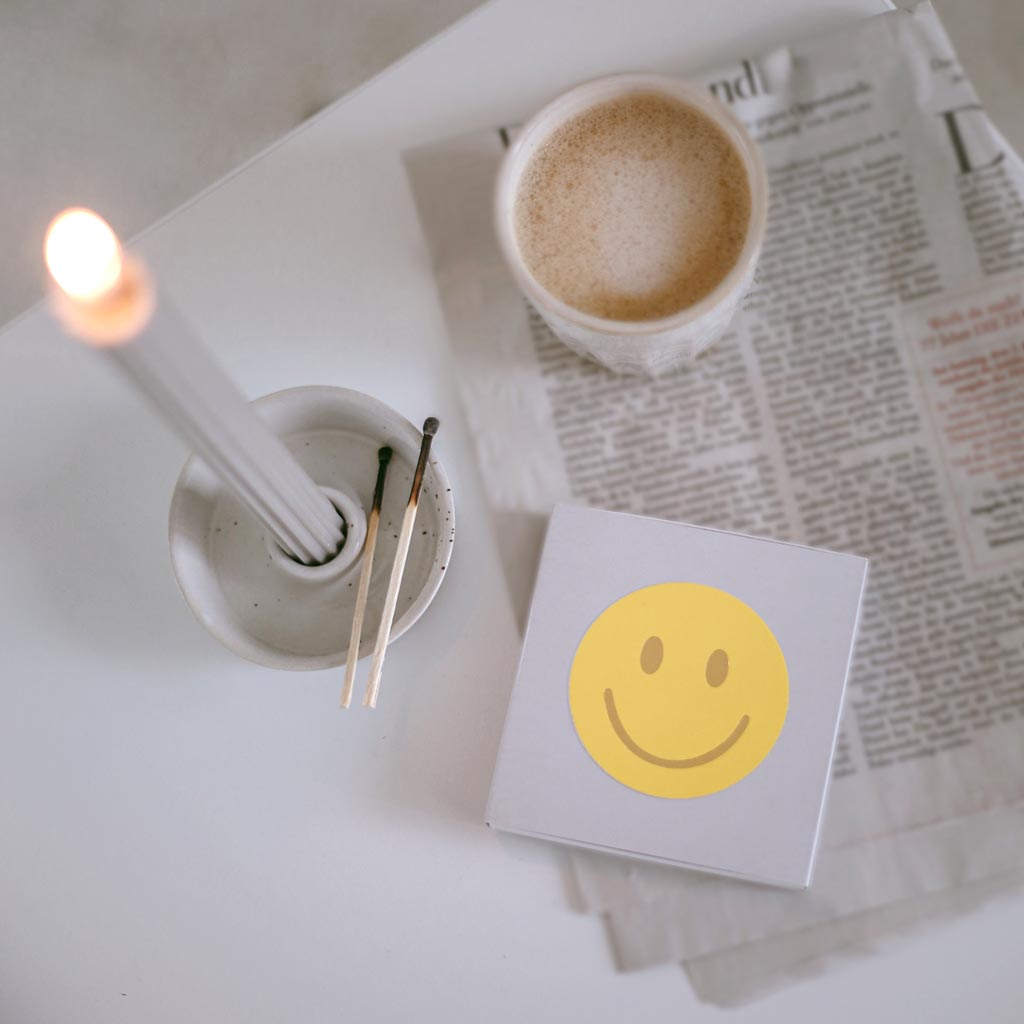 Maxi-Streichhölzer von Eulenschnitt mit Smiley auf der Vorderseite, Moodbild mit brennender Kerze auf einem Tisch